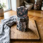Stacked cut soap bars with a marbled clay-pink and charcoal swirl pattern on a wooden cutting board